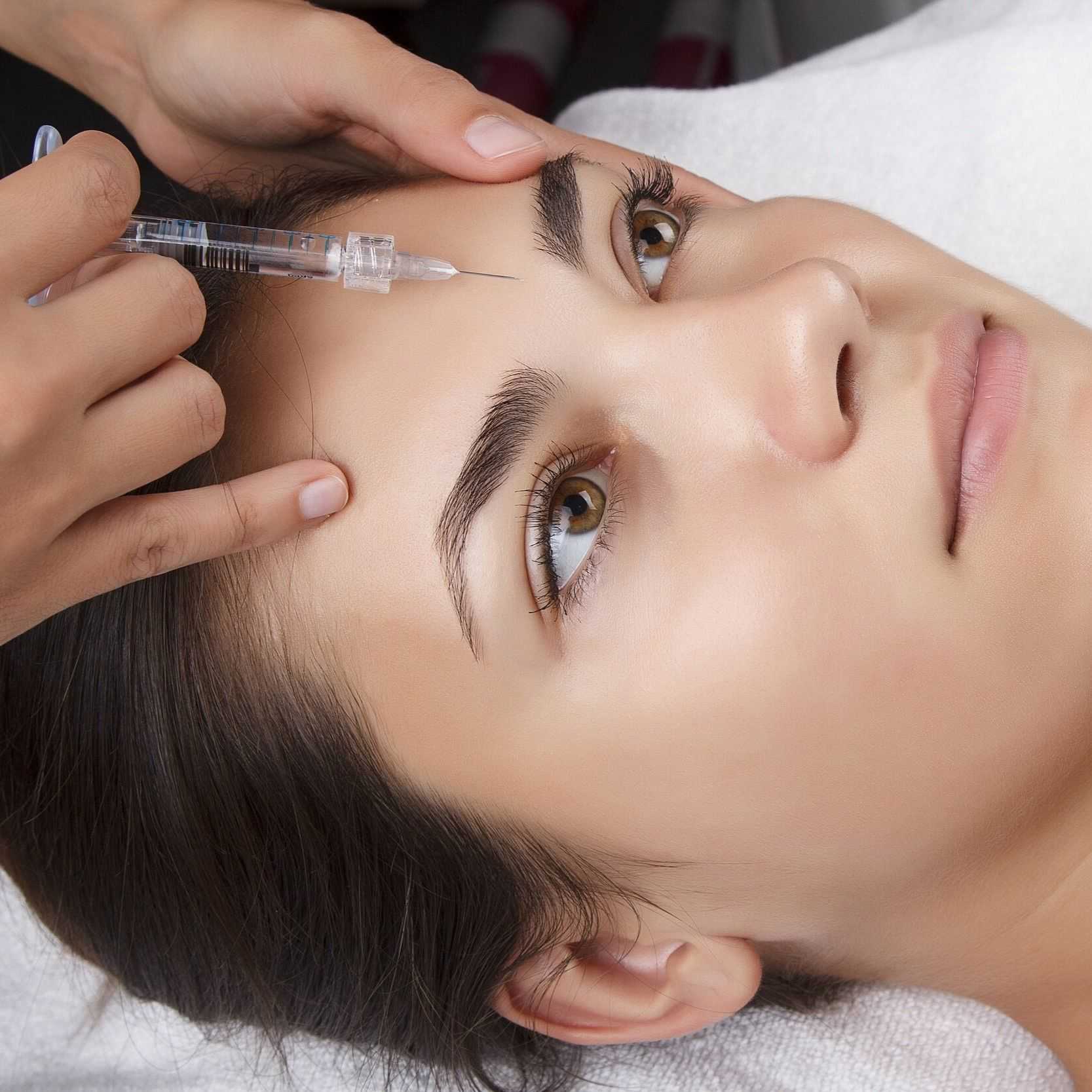 Woman receiving a cosmetic injection in forehead at a skincare clinic.
